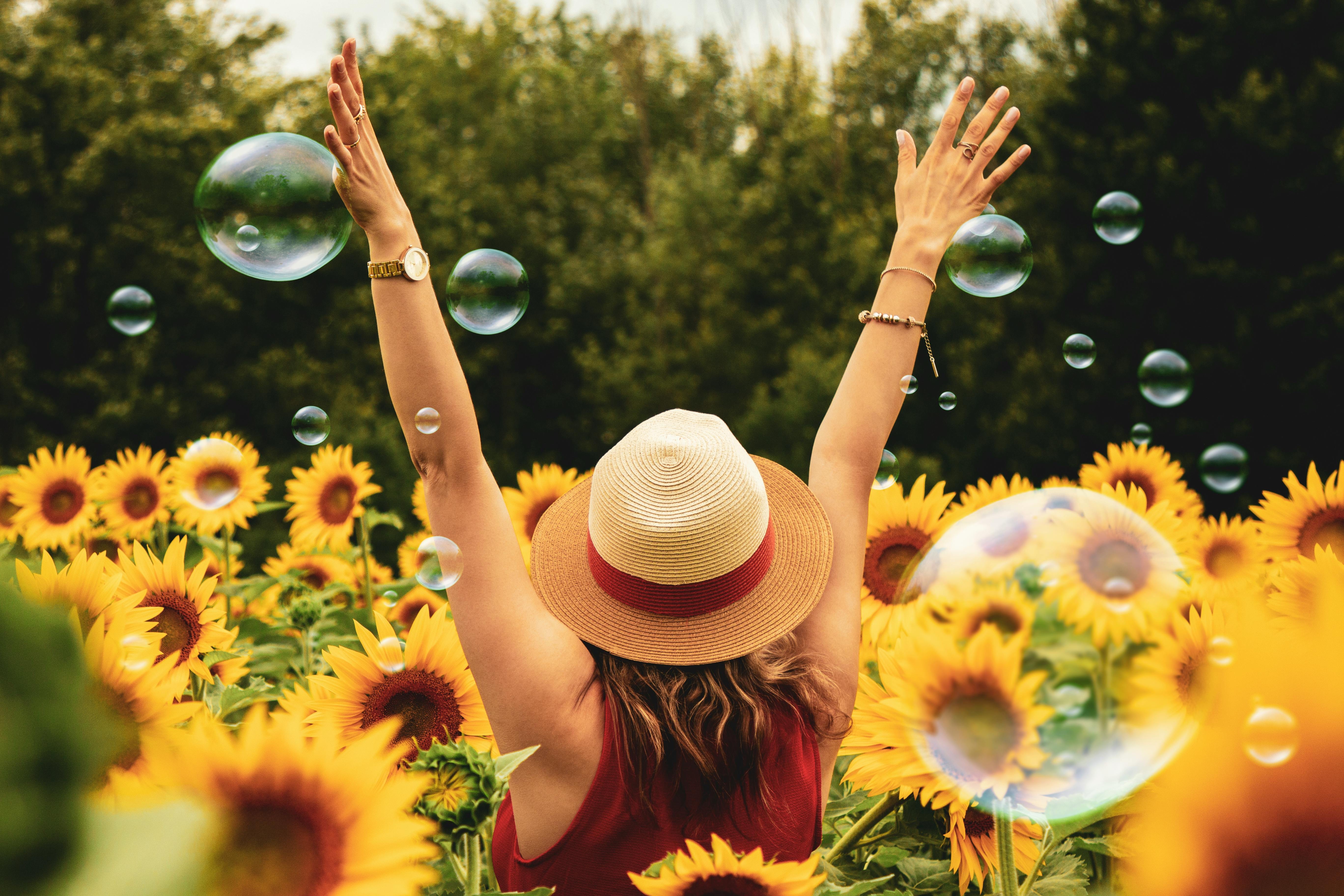 A woman standing joyfully in a field of sunflowers with her hands raised, symbolizing the Shift and Shine clinical EFT package for overcoming motherhood or midlife burnout and menopause symptoms in Charlotte, NC
